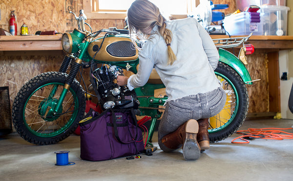 A person working on a motorcycle with The Truck beside them filled with tools.